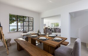 A modern dining area with a wooden table set for six, large windows with a view, and a stone wall. - Villa Terrissa, Divine Sea Views, Private Pool, Furnished Terrace, Arvi (Crete)