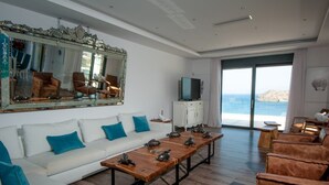 A spacious living room with a white sofa, blue cushions, a wooden coffee table, and a large mirror. - Seafront Villa Astraiax, Divine Sea Views, Private Infinity Pool, Furnished. (Crete)
