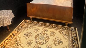 A bedroom with a bed, a small table, a patterned rug, a framed picture, and a window with bars.