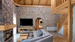 Ein gemütliches Wohnzimmer mit Steinwand, einer Holztreppe und einem Flachbildfernseher.