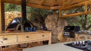 Eine Außenküche mit Steinwand, Holzschränken und einem Grill.