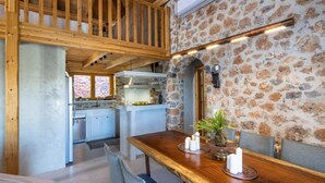 Ein rustikales Interieur mit einem Holztisch, der mit Kerzen gedeckt ist, einer Steinwand und einer Küche im Hintergrund.