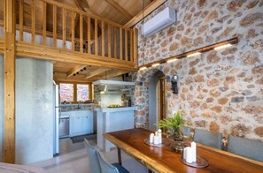 A rustic interior with a wooden dining table set with candles, a stone wall, and a kitchen in the background. - Villa Vireon, Divine Mountain and Nature Views, Private Infinity Pool,. (Crete)