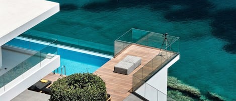 A modern building with a glass balcony overlooking a clear blue pool and turquoise sea.