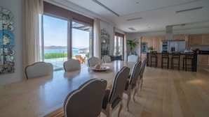 Un vaste espace de salle à manger avec une grande table et des chaises, une cuisine dotée de meubles en bois et une vue sur l’océan.