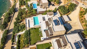 Vue aérienne d’une propriété située sur la côte, dotée d’une piscine, de nombreuses pièces et d’un espace de plage.