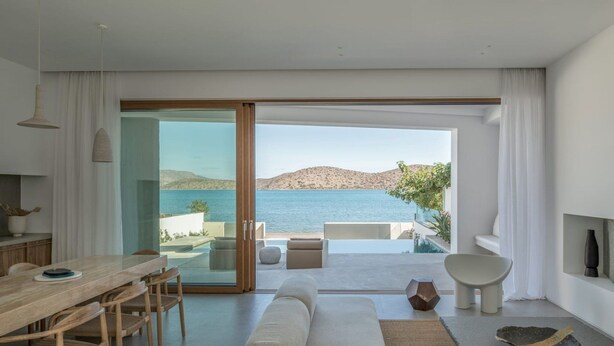 A modern living room with a large sliding glass door leading to a balcony with a view of the sea and hills. - Seafront Villa Noctessa, Divine Sea Views, Private Infinity Pool, Furnished. (Crete)