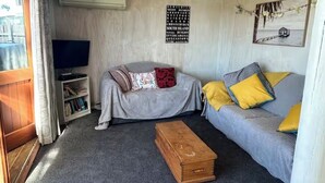 Una sala de estar con un sofá gris, un cofre de madera y un televisor.