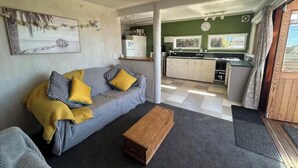 Una sala de estar acogedora con un sofá, una mesa de centro de madera y una cocina visible a través de un umbral abierto.