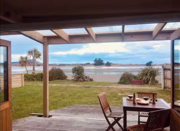 Une terrasse couverte, dotée d’une table et de chaises, qui offre une vue sur une plage et l’océan.