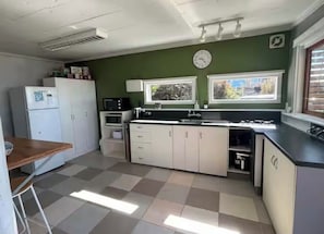 Une cuisine avec un carrelage à motifs, des placards blancs, un four à micro-ondes, un réfrigérateur et deux fenêtres équipées de stores.