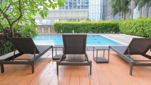 A poolside area with three wicker lounge chairs and a small table, surrounded by a wooden deck and greenery. - New! Comfortable 2BR in Central BGC w/ Fast WiFi (G3W2+RG Taguig, Metro Manila, Philippines)