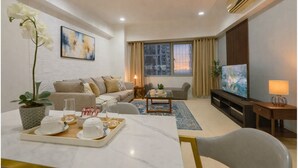 A modern living room with a sofa, a coffee table, a TV, and a dining area with a tray of cups and saucers. - New! Comfortable 2BR in Central BGC w/ Fast WiFi (G3W2+RG Taguig, Metro Manila, Philippines)