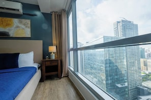 A hotel room with a bed, a nightstand, a lamp, a window with a city view, and an air conditioning unit. - New! Comfortable 2BR in Central BGC w/ Fast WiFi (G3W2+RG Taguig, Metro Manila, Philippines)