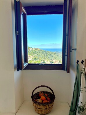 A room with a window overlooking a coastal landscape, a wicker basket with oranges on the floor, and a green curtain. - Top floor, 3 double bedrooms, roof top, fabulous sea, mountain and village views (Santa-Reparata-di-Balagna)