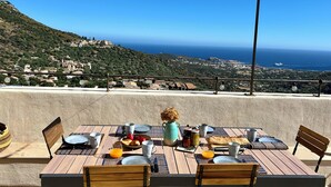 Une table dressée pour le petit-déjeuner, avec vue sur la mer et sur une ville perchée sur une colline.
