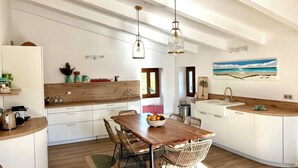 Une cuisine moderne avec des meubles blancs, des plans de travail en bois et un coin repas comprenant une table en bois et des chaises en osier.