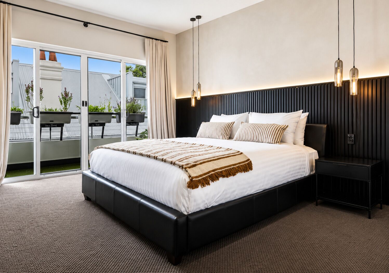 Une chambre moderne avec un grand lit, une table de chevet, un luminaire au plafond et une vue sur l’extérieur grâce à une porte coulissante.