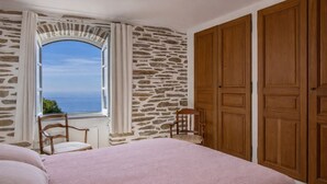 Ein Schlafzimmer mit Steinwand, einem großen Fenster mit Aussicht, einem Bett mit rosa Bettdecke und Holzschränken.