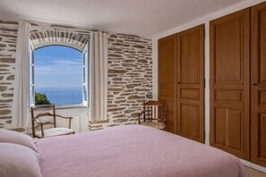 Ein Schlafzimmer mit Steinwand, einem großen Fenster mit Aussicht, einem Bett mit rosa Bettdecke und Holzschränken.