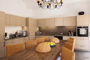 Eine moderne Küche mit Holzausstattung, einem Esstisch mit Korbstühlen und einer Kronleuchter.
