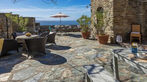 Eine Terrasse im Freien mit Steinboden, Korbmöbeln und einem Tisch mit einem blauen Behälter.