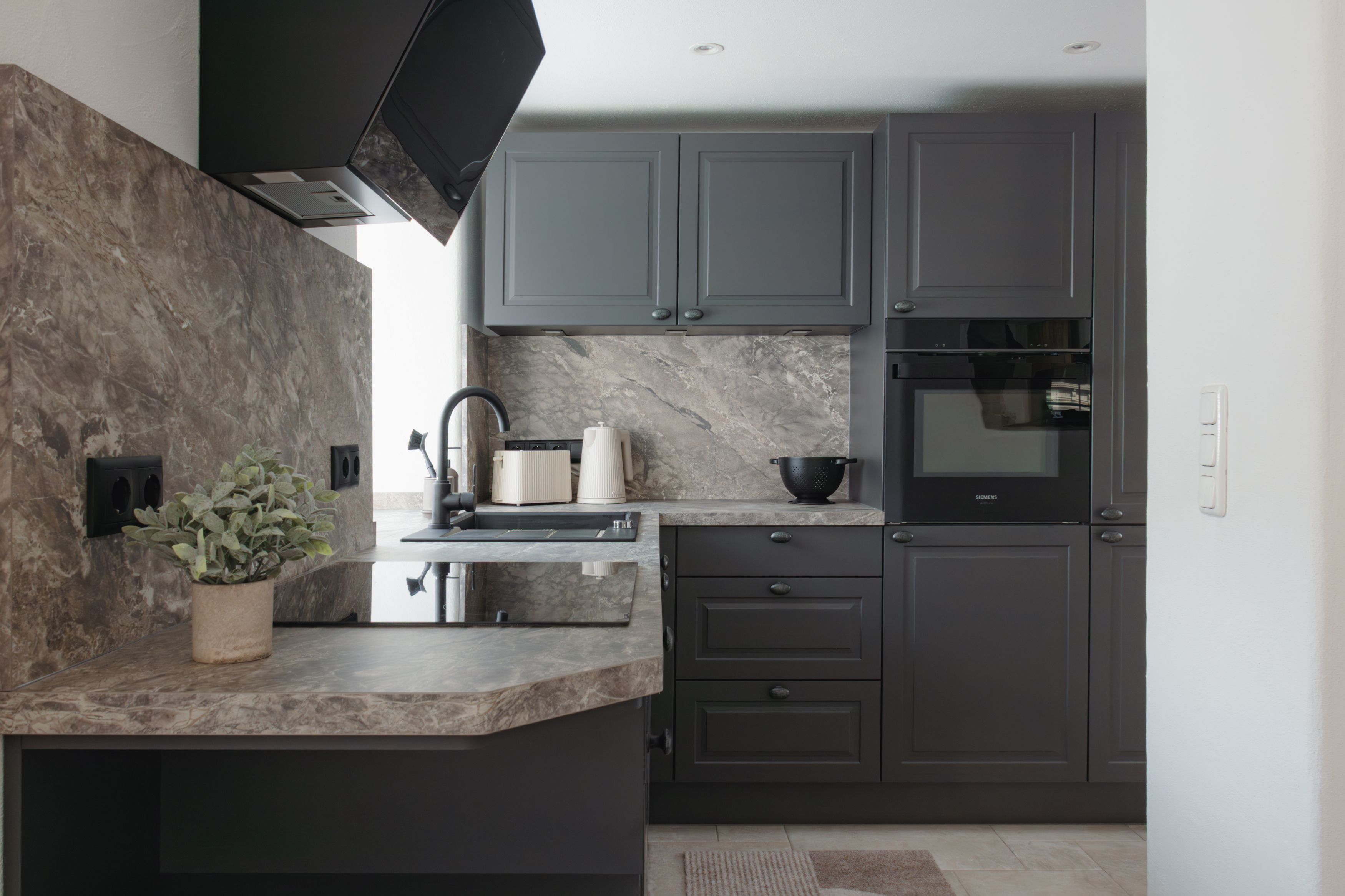 Une cuisine moderne avec des meubles de couleur sombre, un plan de travail en marbre et un four encastré.