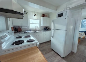 Een moderne keuken met witte apparaten, een houten tafel en een raam dat natuurlijk licht binnenlaat.
