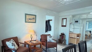 Una sala de estar con dos sillones de cuero marrón, una mesa de centro de madera y una lámpara. En el fondo, se ve una mesa de comedor con sillas.