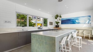 A modern kitchen with a large island, bar stools, a potted plant, and a view of the outdoors through large windows. - Beach Haven Getaway Broadbeach - WiFi, Parking (Broadbeach)