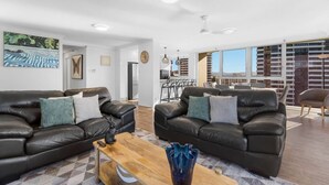 A spacious living room with two leather sofas, a wooden coffee table, and a large window offering a city view. - Beach Haven Getaway Broadbeach - WiFi, Parking (Broadbeach)