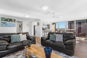 A spacious living room with two leather sofas, a wooden coffee table, and a large window offering a city view. - Beach Haven Getaway Broadbeach - WiFi, Parking (Broadbeach)