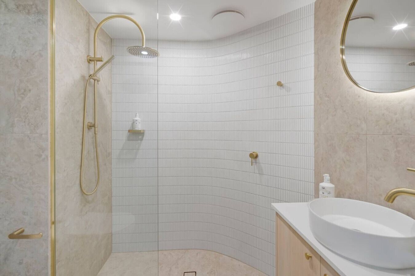 A modern bathroom with a corner shower, white tiled walls, and a vanity with a sink.