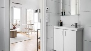 Un baño moderno con muebles blancos, un espejo grande y piso de baldosas.