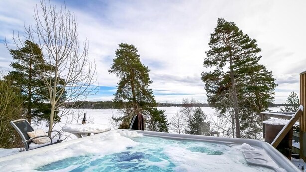 Un jacuzzi rodeado de árboles cubiertos de nieve y una vista de un lago.
