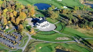 Un campo de golf con club house, zona de estacionamiento y árboles circundantes.