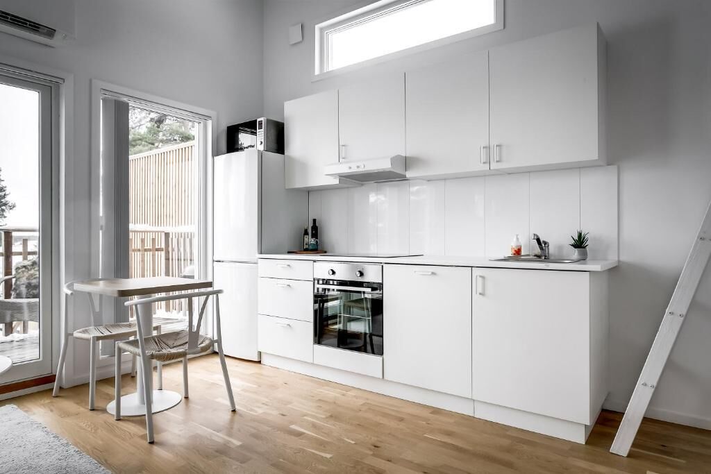A modern kitchen with white cabinetry, a built-in oven, and a dining area with a table and chairs.