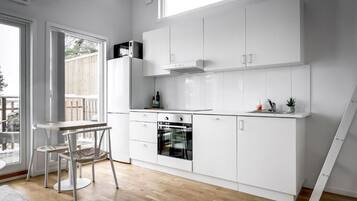 A modern kitchen with white cabinetry, a built-in oven, and a dining area with a table and chairs.