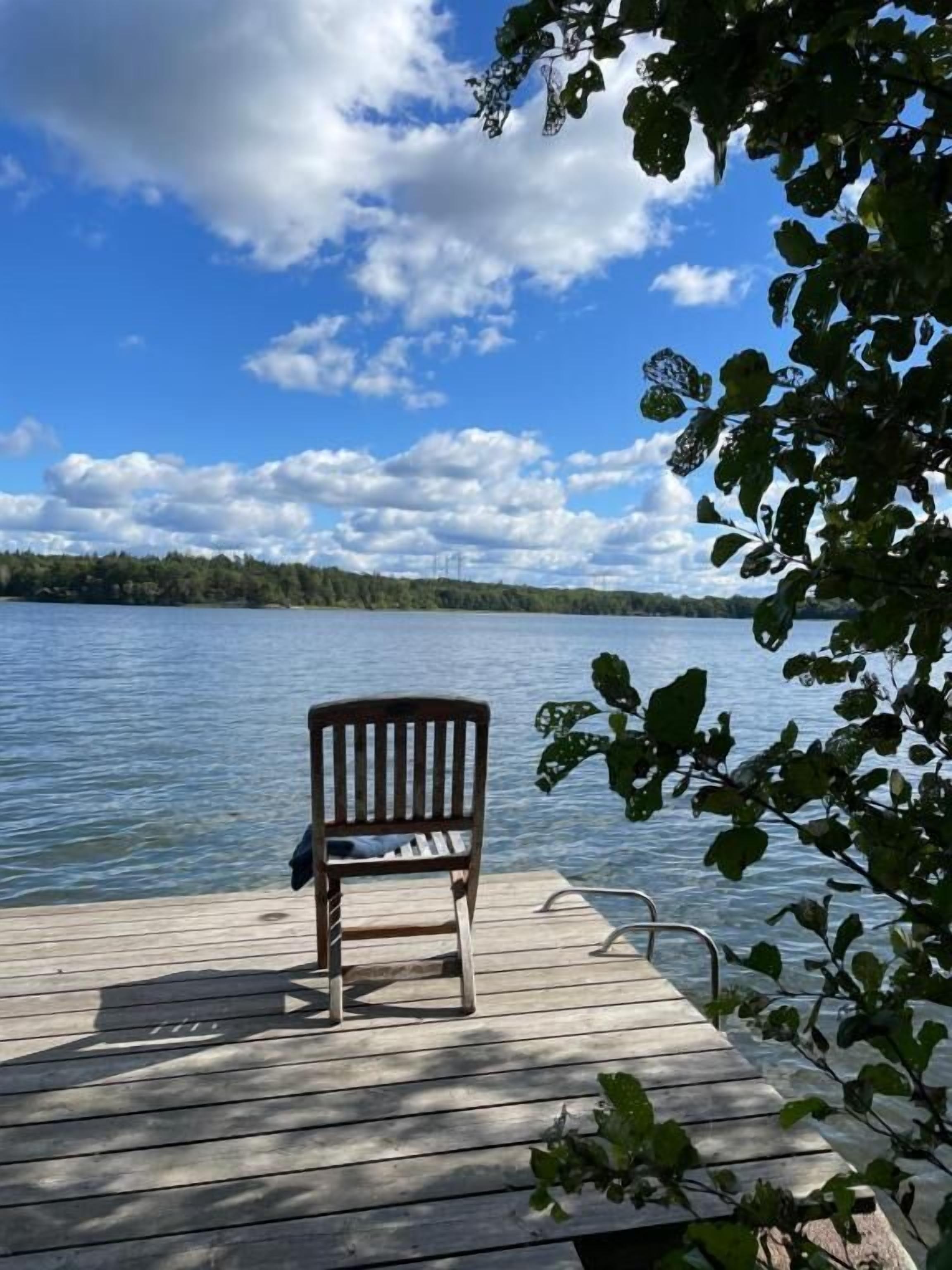Una banchina in legno che si estende in un lago calmo, con cielo sereno e una riva boscosa in lontananza.