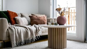 Una sala de estar acogedora con un sofá, una mesita redonda y un jarrón con plantas secas.