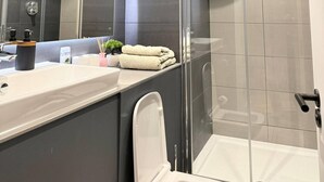 Ein modernes Badezimmer mit einer Duschkabine aus Glas, einem großen Spiegel und einem Waschtisch mit Spüle und Handtuchhalter.