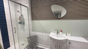 Ett modernt badrum med en duschavdelning med glasväggar, en vit tvättställ och en väggpanel av trä.