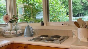 A kitchen with wooden cabinets, a gas stove, and a window with a view of greenery. - Berry Lodge- A Sweet Country Escape! (Jamieson)