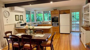 A modern kitchen with wooden cabinets, a central island, and a dining area with a wooden table and chairs. - Berry Lodge- A Sweet Country Escape! (Jamieson)