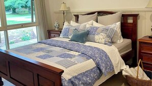 A bedroom with a wooden bed, a ceiling fan, a window with a view of greenery, and a bedside table with a lamp. - Berry Lodge- A Sweet Country Escape! (Jamieson)