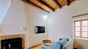 Ein Wohnzimmer mit Kamin, einem blauen Sofa, einem an der Wand befestigten Fernseher und einem Fenster mit Jalousien.
