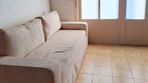 Ein Zimmer mit einem beigen Sofa, einem Fliesenboden und einem großen Rundbogenfenster.
