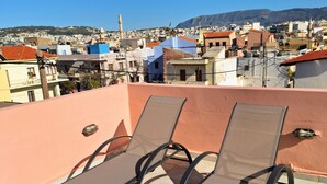 Eine Dachterrasse mit zwei Liegestühlen, freier Blick auf eine Stadtlandschaft und ein entferntes Gebirge.