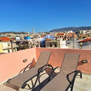 Una terraza en la azotea con dos sillones de descanso, vistas despejadas de la ciudad y una montaña distante.
