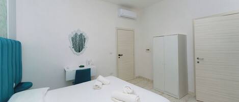 A hotel room with a bed, a desk, a mirror, an air conditioning unit, and two wardrobes.